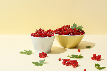 Bowls with fresh red currants and leaves on color background