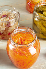 Pickled carrot in a glass jar, sauerkraut, and gherkings on a rustic wooden background. Canning fermented food