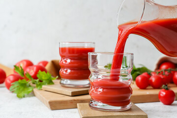 Pouring tasty tomato juice from jug into glass on light background
