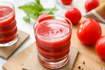 Glasses of tasty tomato juice on light background