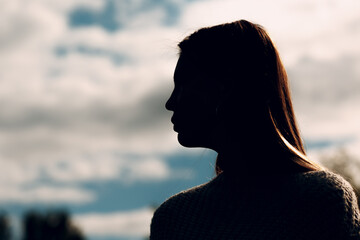 Pretty young woman outdoor in the park at summer. Silhouette portrait with sky