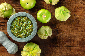 Tomatillos, green tomatoes, with salsa verde, green sauce, in a molcajete, traditional Mexican mortar, overhead flat lay shot with a place for text - obrazy, fototapety, plakaty