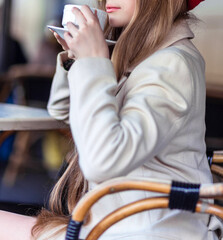 Young woman in trench coat and dress holds coffee cup and enjoys morning