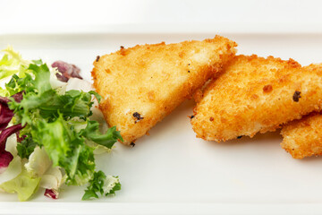 Pieces of fried cheese with lettuce on a white plate. Appetizing starter. Close-up.