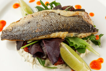 Fried fish with vegetables. Appetizing dish with sauce on a white plate. Close-up.