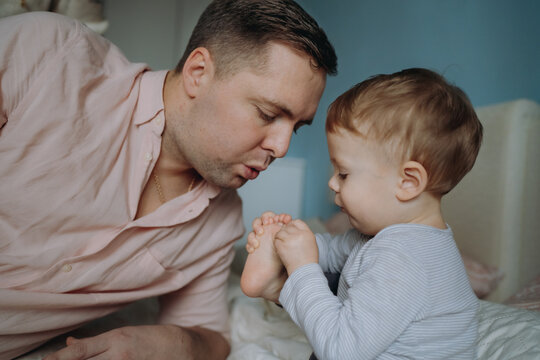 father and son. Man blowing on son's toe to cool down and ease pain. Image with selective focus