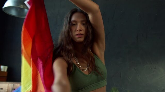 Young girl dances with LGBTQ rainbow flag in a studio with black wall and big window