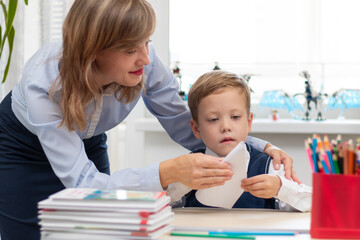 A beautiful young mother with her son makes a paper airplane while isolated on a light wooden table. Selective focus. Portrait
