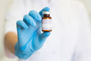 close-up of a hand in a blue  medical glove holds a brown mudic vial with a medicine for injection...