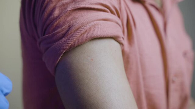 Close up of doctor or nurse hands pasting covid-19 vaccination booster shot bandage to shoulder - concpet of coronavirus 3rd dose for immunocompromised people.