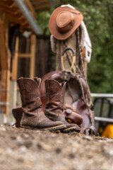 Ranch life scenery: muddy western boots in front of a western saddle. Cowboy boots. Muddy working boots