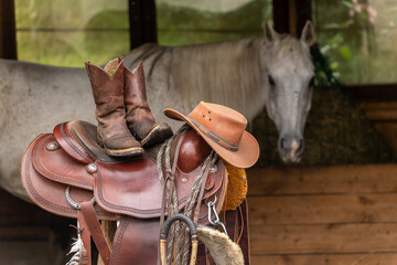 Equipment for western riding in front of a horse. A Western saddle, boots and a cowboy hat with a...