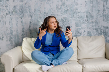 angry beautiful woman sitting on the couch with mobile phone. Woman going crazy over something on her phone. Annoyed young woman looking at mobile phone screen, feeling nervous. Angry lady.