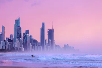 Deurstickers Lichtroze Sunlit skies over Surfers Paradise cityscape, with surfer going into the ocean