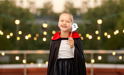 halloween, holiday and childhood concept - happy smiling girl in black dracula costume with cape...