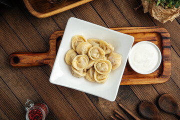 Russian pelmenii dumplings with sour cream on wooden background