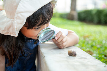 Happy kid girl exploring nature with a magnifying glass and a snail. He having fun in the garden. The concept of the kid is ready to go to school.