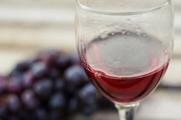 Glass of red wine with a bunch of grapes on wooden background, close up