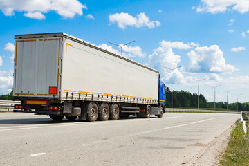 A heavy-duty vehicle with a semitrailer drives along the highway on a summer day.