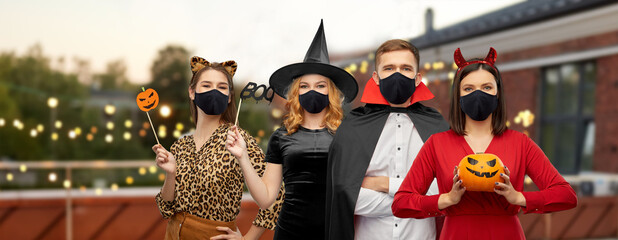 holiday, health and pandemic concept - friends in halloween costumes and black reusable masks over...