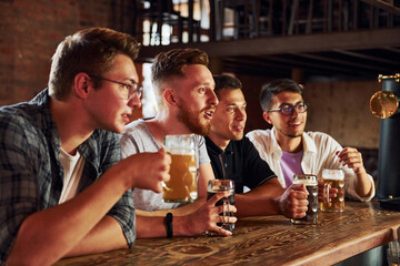 With beer in hands. People in casual clothes sitting in the pub