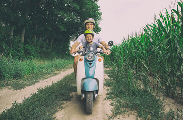 The father and son riding together through the field by pathway on the retro scooter - Powered by Adobe