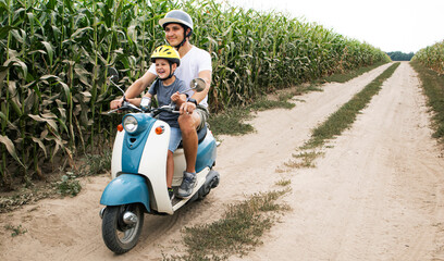 The father and son riding together through the field by pathway on the retro scooter © SkyLine