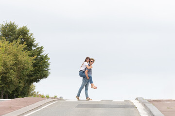 Romantic couple crossing the road. Young man carrying on his back or piggyback girlfriend. Minimal composition with copy space.