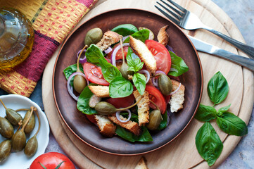 Italian Panzanella salad with bread, tomatoes, basil, capers and olive oil on brown background. Top view