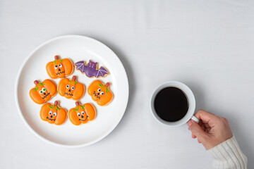 Obraz na płótnie Canvas woman hand holding coffee cup during eating funny Halloween Cookies. Happy Halloween day, Trick or Threat, Hello October, fall autumn, Traditional, party and holiday concept