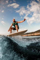 sportsman on wakeboard while skilfully jumping over splashing river wave against blue sky.