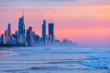 Surfer in the ocean with Gold Coast skyline at sunrise.