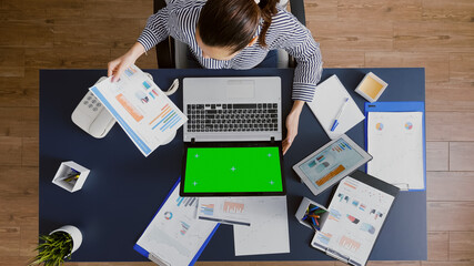 Top view of manager woman working at management strategy looking at mock up green screen chroma key laptop with isolated display in startup office. Businesswoman analyzing company accounting paperwork