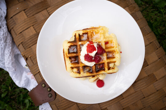Waffles on the white plate on brown wood basket. Eating outside, picnic.