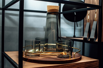 Tray with stylish dark glass decanter and glasses on the shelf. Empty transparent carafe with...