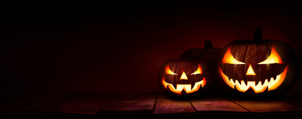 Three scary halloween lanterns with evil eyes and faces on a rustic wood table with a spooky dark...