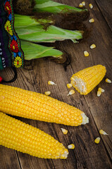 Two raw maize without leaves and bag with corn on wooden table