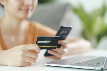 Young woman holding credit card and using smart phone for online shopping, internet banking, e-commerce, spending money, working from home concept
