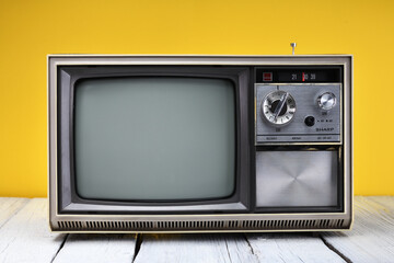 An old vintage television set from the 1970s stands on a wooden table against a yellow background....
