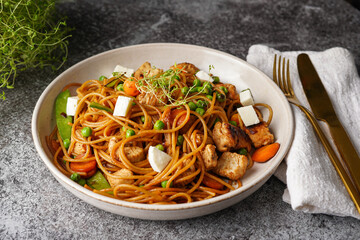 Italian pasta spaghetti with chicken, green beans and cheese mozzarella and fresh thyme in light grey bowl on grey concrete surface, golden silverware and beige colored napkin