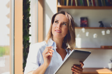 Portrait of businesswoman with e-book, tablet next to window in room