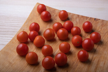 Tasty little red cherry tomatoes, just washed, with drops of water, on a beautiful unusual wooden platter.