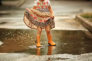 little girl near the puddle in yellow rubber boots