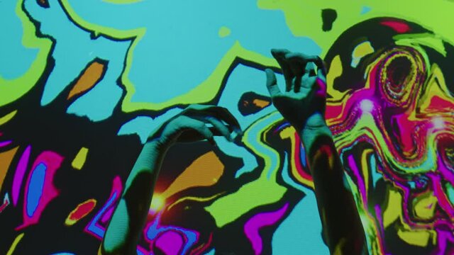Beautiful female hands moving slowly on neon abstract background. Girl shows arms dance near multicolored wall illumination. Nightclub performance under luminous light metamorphoses