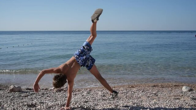 summer outdoor beach activity of little kid making somersault on pebble sea shore during season vacation holiday travel