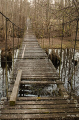 Old and damaged rope and wooden boards bridge over the river Irbe, Latvia.