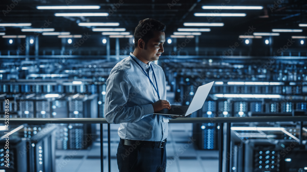 Poster Portrait of IT Specialist Uses Laptop in Data Center. Server Farm Cloud Computing Facility with Male Maintenance Administrator Working. Cyber Security and Network Protection.