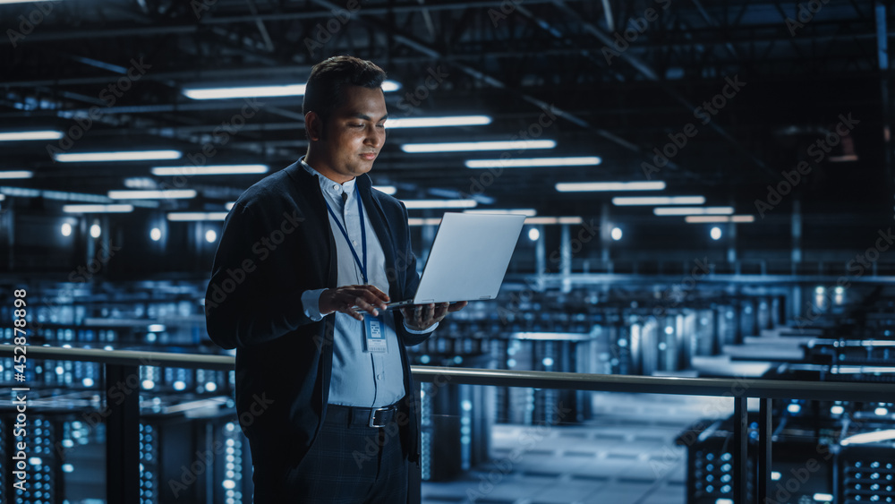 Fototapete Portrait of IT Specialist Uses Laptop in Data Center. Server Farm Cloud Computing Facility with Male System Administrator Working. Cyber Security and Network Protection.