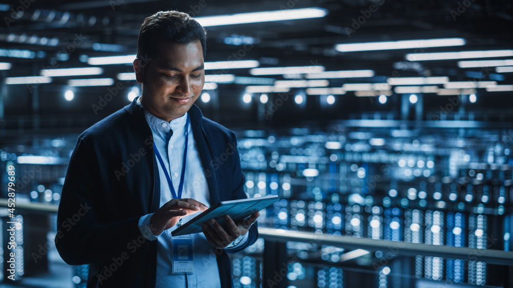 Poster Handsome Smiling IT Specialist Using Tablet Computer in Data Center. Succesful Businessman and e-Business Entrepreneur Overlooking Server Farm Cloud Computing Facility.