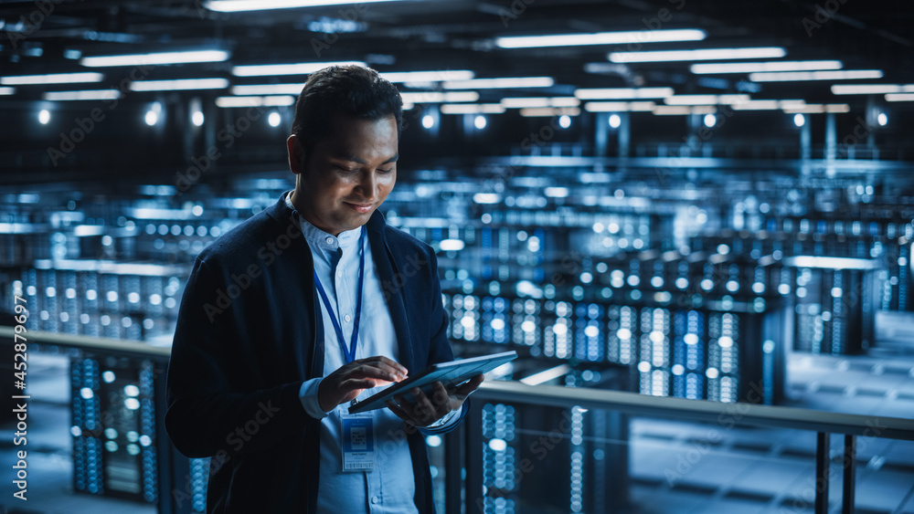Poster Handsome Smiling IT Specialist Using Tablet Computer in Data Center. Succesful Businessman and e-Business Entrepreneur Overlooking Server Farm Cloud Computing Facility.